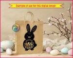 Black silhouette image of an adorable Easter bunny full of springtime charm. The bunny has tall floppy ears, a round chubby body, and a sweet little face that feels friendly and playful. It holds a woven basket packed with colorful Easter eggs, each one softly rounded and cheerful. The bold silhouette is accented with simple details, giving it a cute folk-art look that pops beautifully.