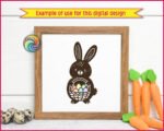 Black silhouette image of an adorable Easter bunny full of springtime charm. The bunny has tall floppy ears, a round chubby body, and a sweet little face that feels friendly and playful. It holds a woven basket packed with colorful Easter eggs, each one softly rounded and cheerful. The bold silhouette is accented with simple details, giving it a cute folk-art look that pops beautifully.